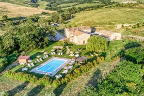 Vista aérea de una propiedad campestre con piscina, sillas de descanso y un edificio de piedra.