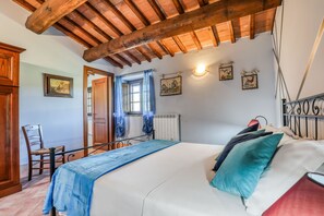 Un dormitorio con techo de madera, una cama con colcha azul, una silla y una ventana con cortinas.
