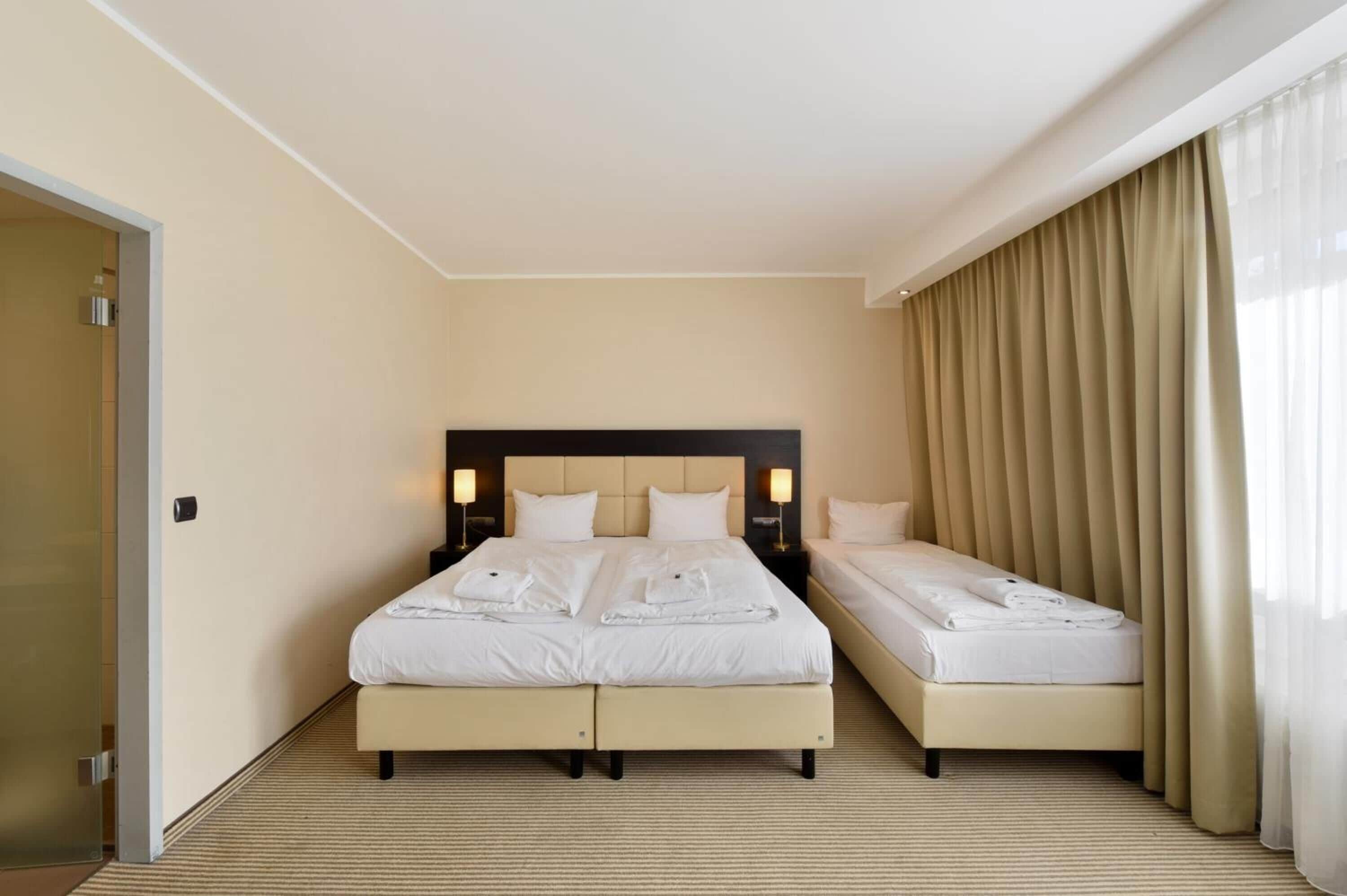 A hotel room with two beds, a large window with curtains, and a door.