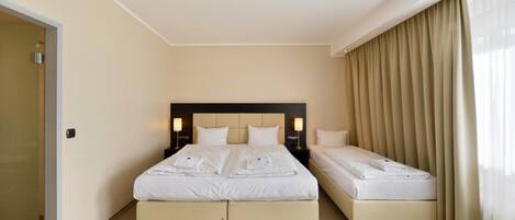 Una habitación de hotel con dos camas, un ventanal con cortinas y una puerta.