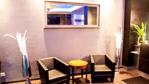 A modern room with two leather armchairs, a small wooden table, and two tall vases with white flowers. A mirror hangs on the wall above the table. - Hotel am Karlstor (Karlsruhe)