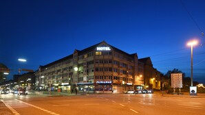 A hotel with multiple floors, a prominent sign, and a street view with cars and a pedestrian crossing. - Hotel am Karlstor (Karlsruhe)