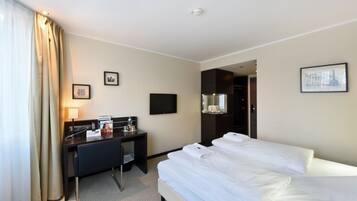 Une chambre d’hôtel avec un lit, un bureau, une chaise, une télévision et une salle de bain visible à travers une porte ouverte.