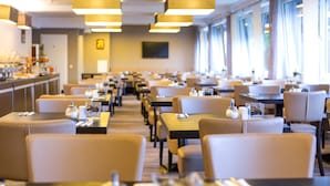 A hotel dining area with rows of tables and chairs, overhead lighting, and large windows. - Hotel am Karlstor (Karlsruhe)