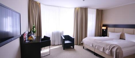 A hotel room with a bed, a desk, a chair, and a television.
