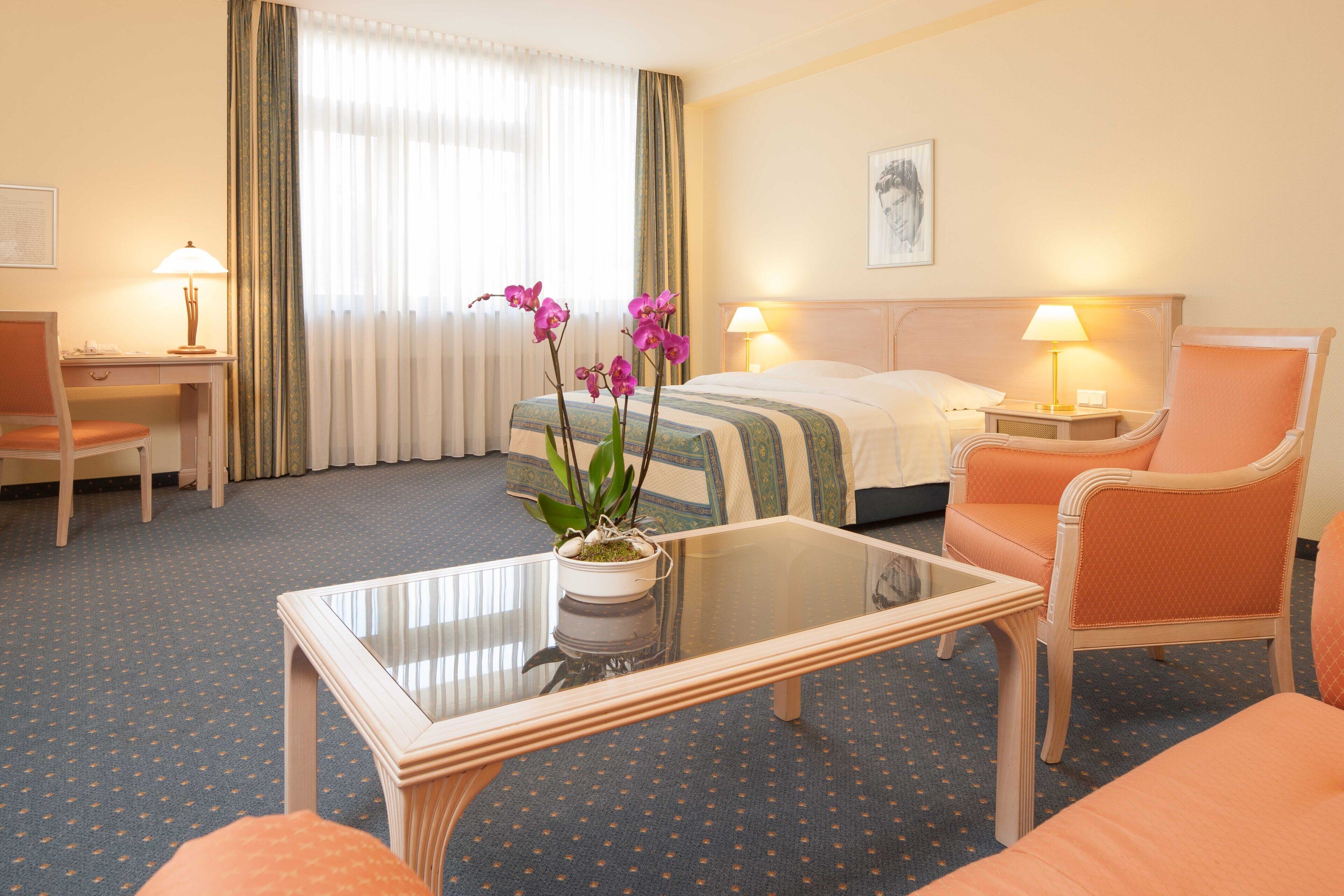 A hotel room with a bed, two chairs, a desk, and a coffee table.