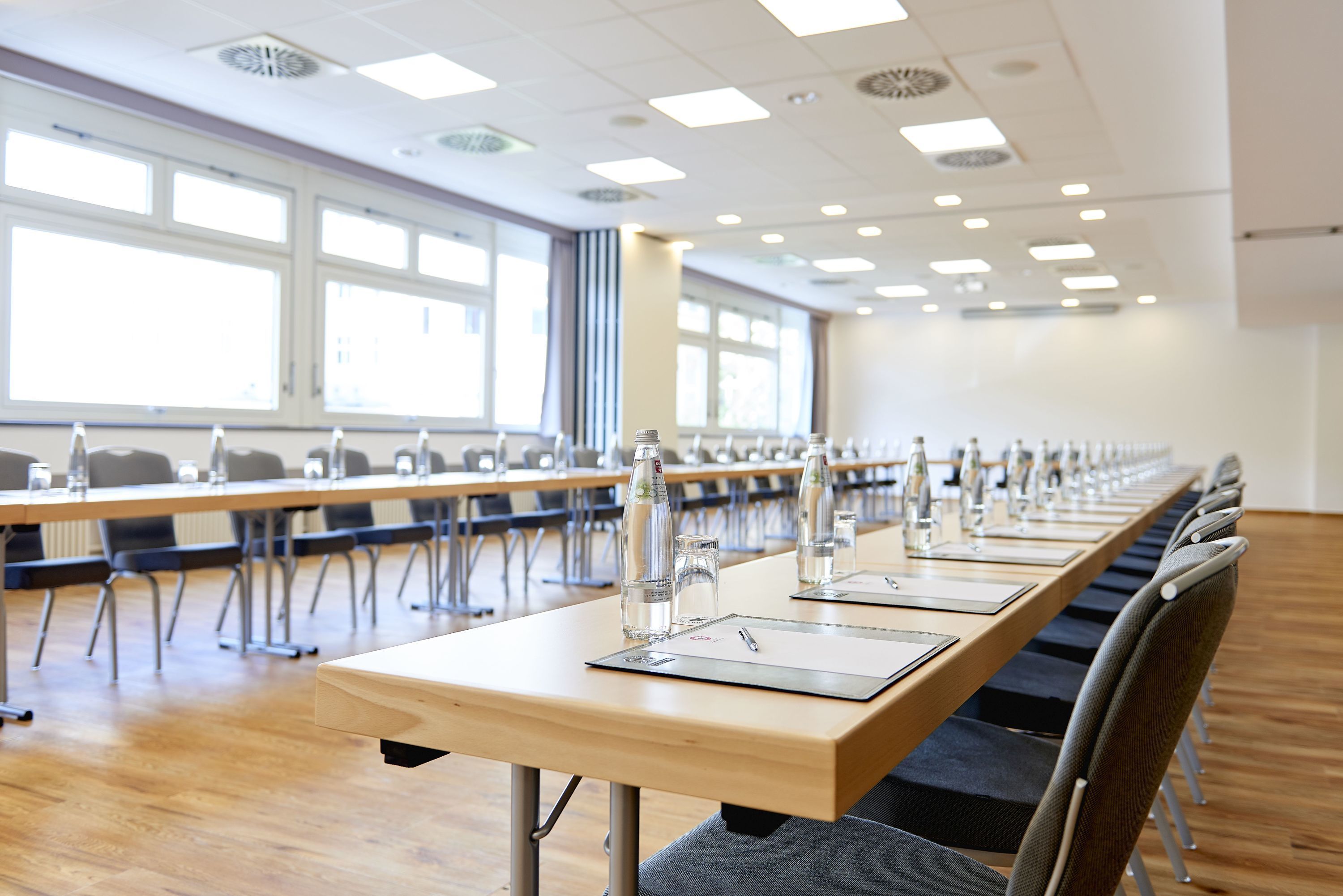 Un salón de conferencias con mesas largas, sillas y botellas de agua.