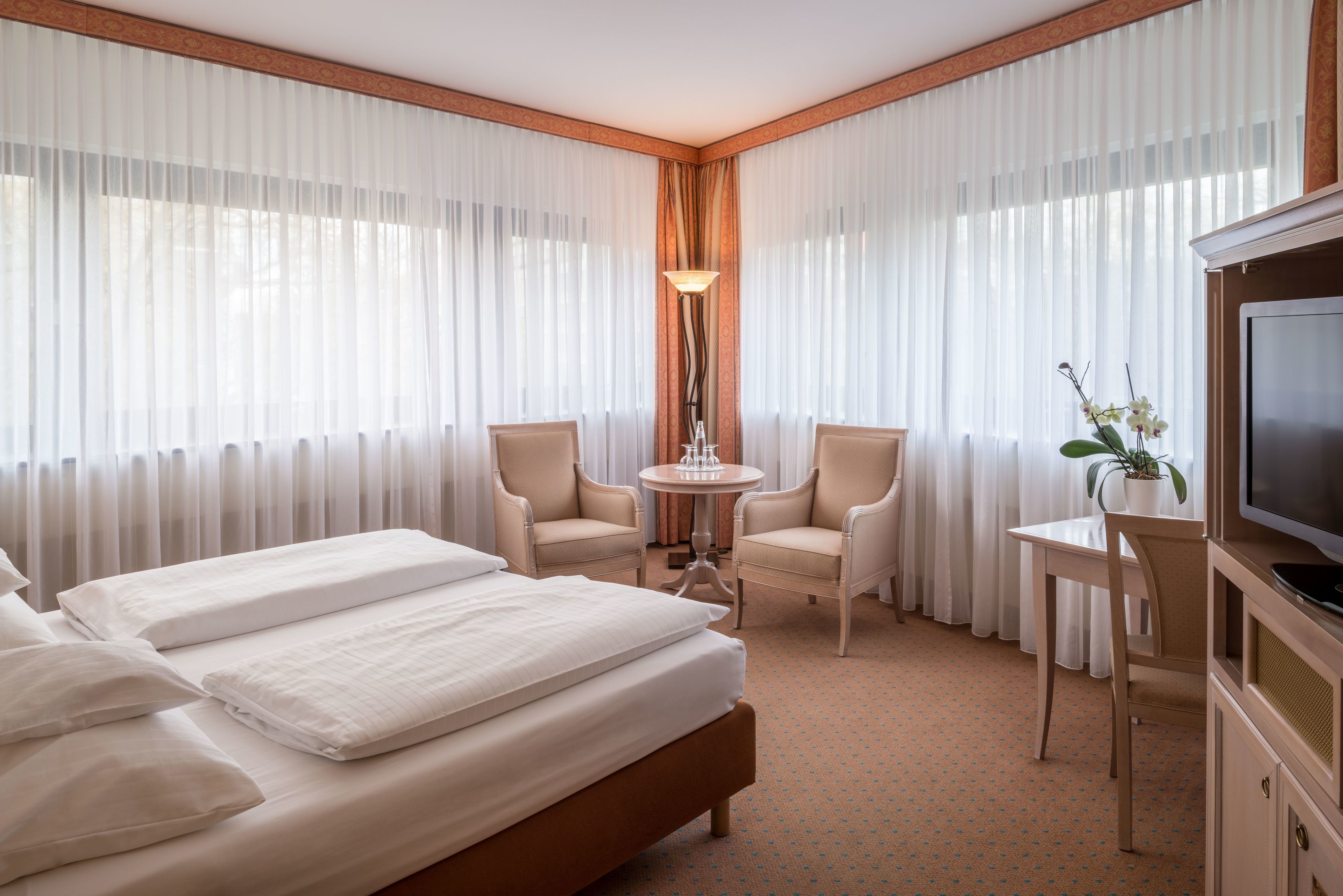 A hotel room with a bed, two chairs, a small table, a TV, and a lamp.