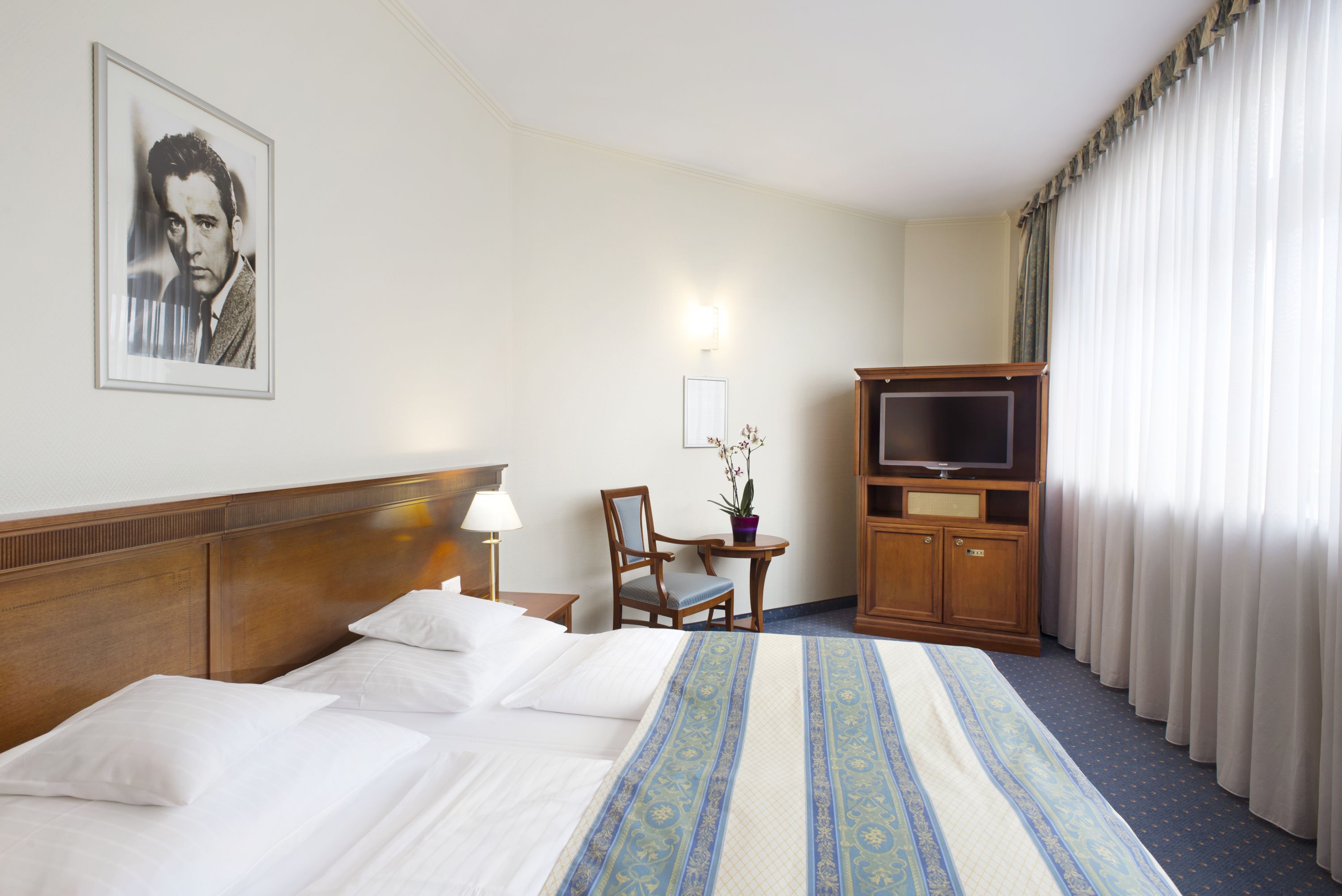 Una habitación de hotel con una cama grande, televisión, escritorio con silla y un cuadro en la pared.