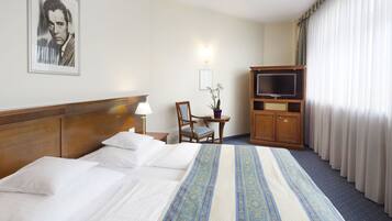 Una habitación de hotel con una cama grande, televisión, escritorio con silla y un cuadro en la pared.