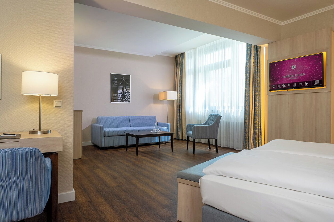 A hotel room with a bed, a sofa, a chair, a desk, and a TV.