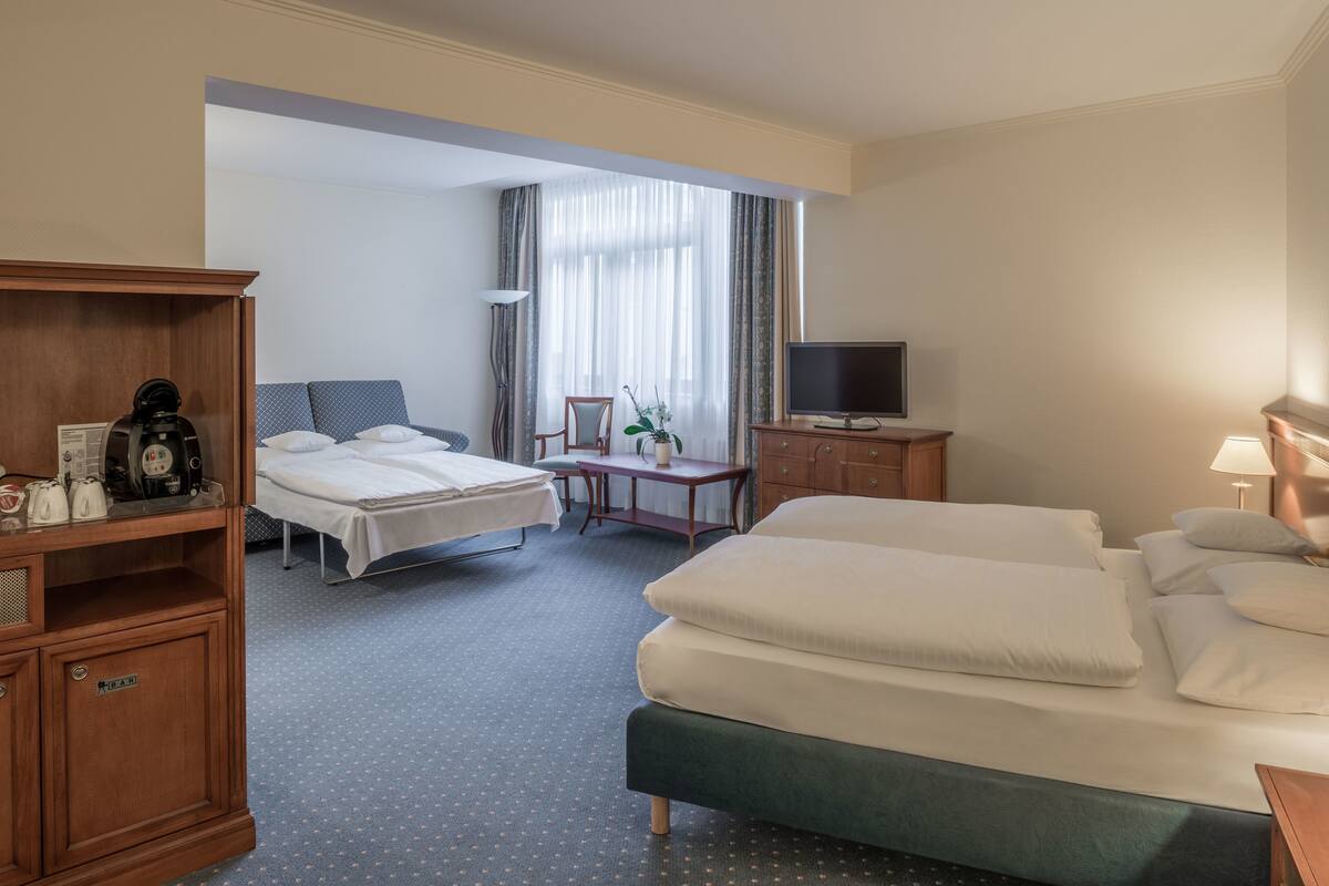 Quarto de hotel com duas camas, uma televisão, uma escrivaninha com cadeira e um armário de madeira.