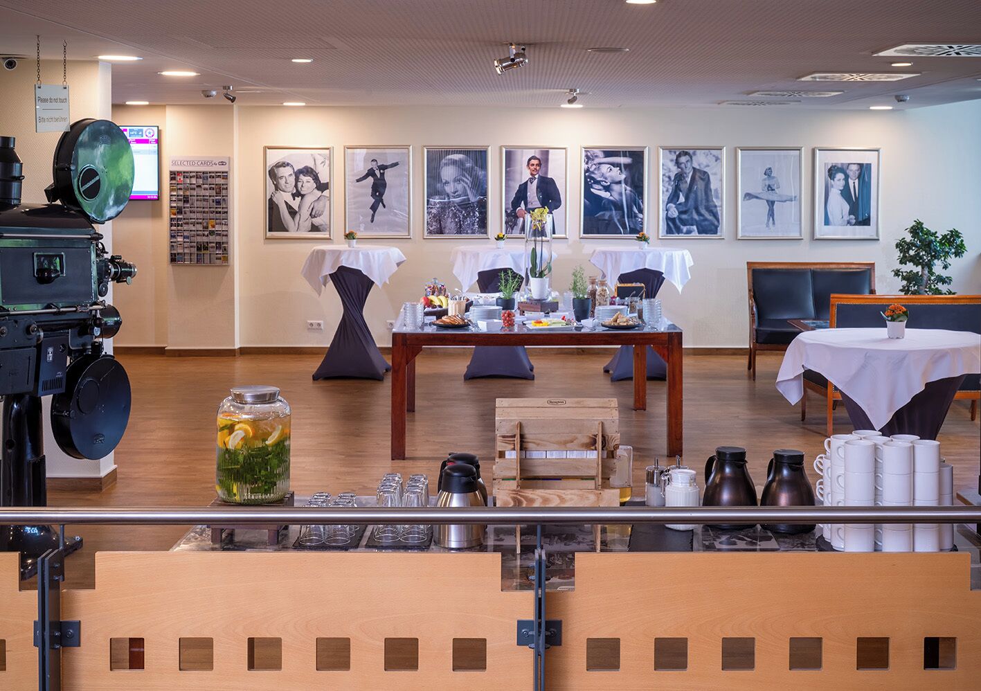 A room with a table set for a meal, framed pictures on the wall, and a camera on a tripod.