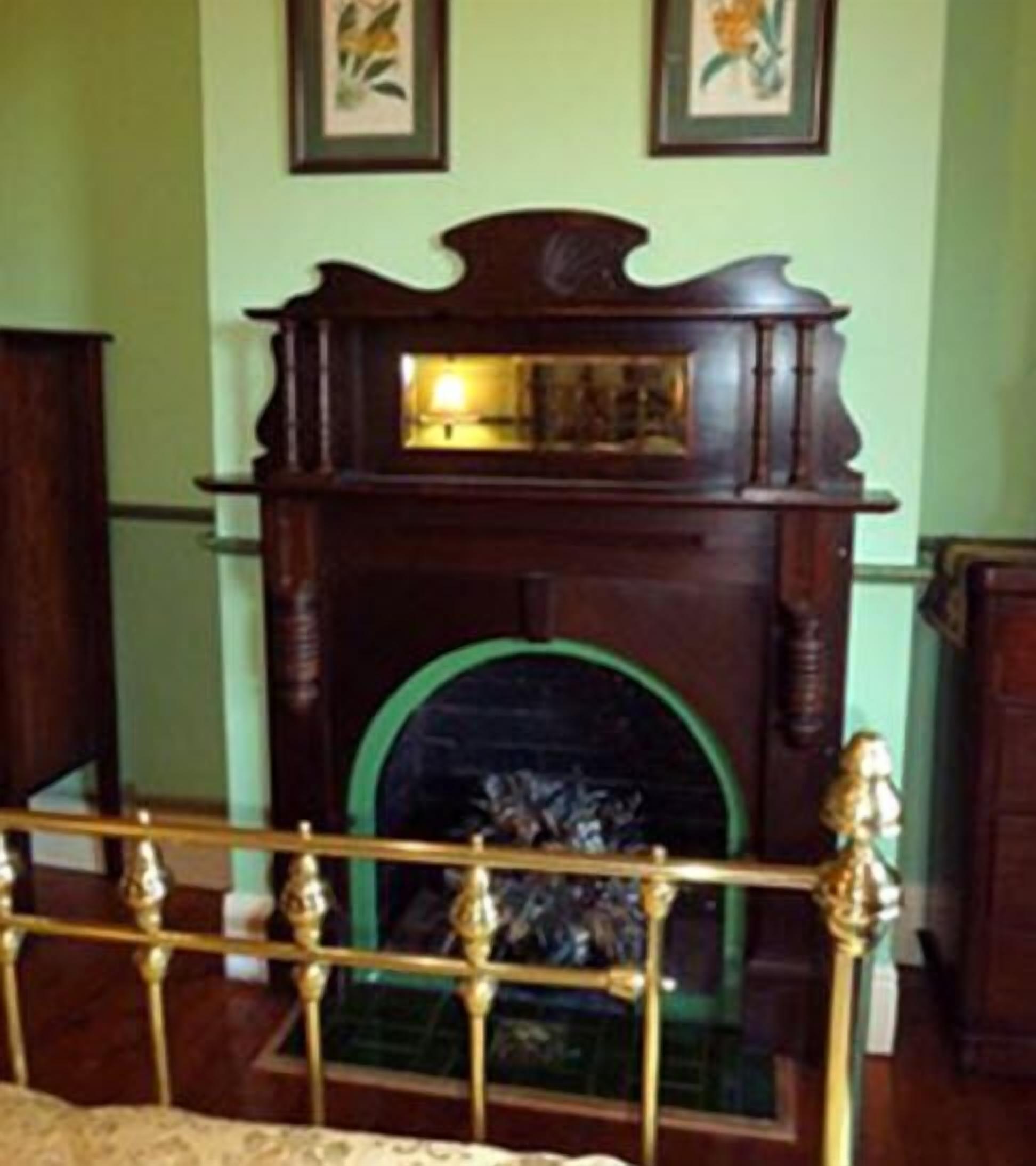 A room with a wooden fireplace, a bed with a headboard, and green walls.