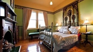 A bedroom with a bed, a window, a lamp, and a fireplace. - The Duck House (Burnie)