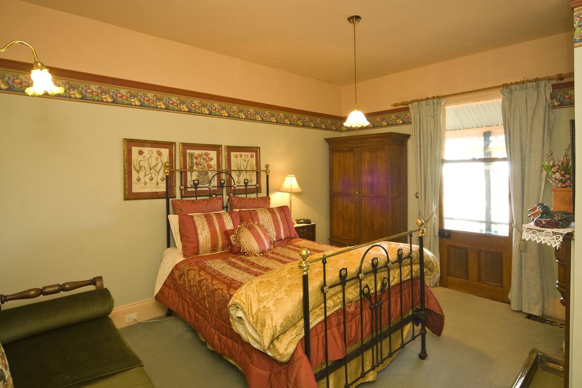 A traditional bedroom with a four-poster bed, a wooden wardrobe, and a window with curtains.