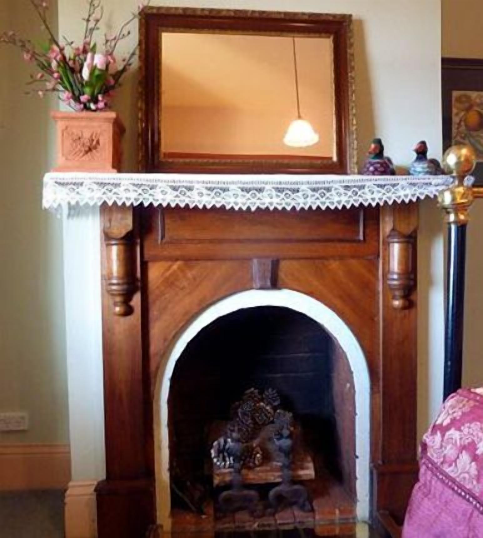 A fireplace with a wooden mantel, a lace trim, and a small statue.