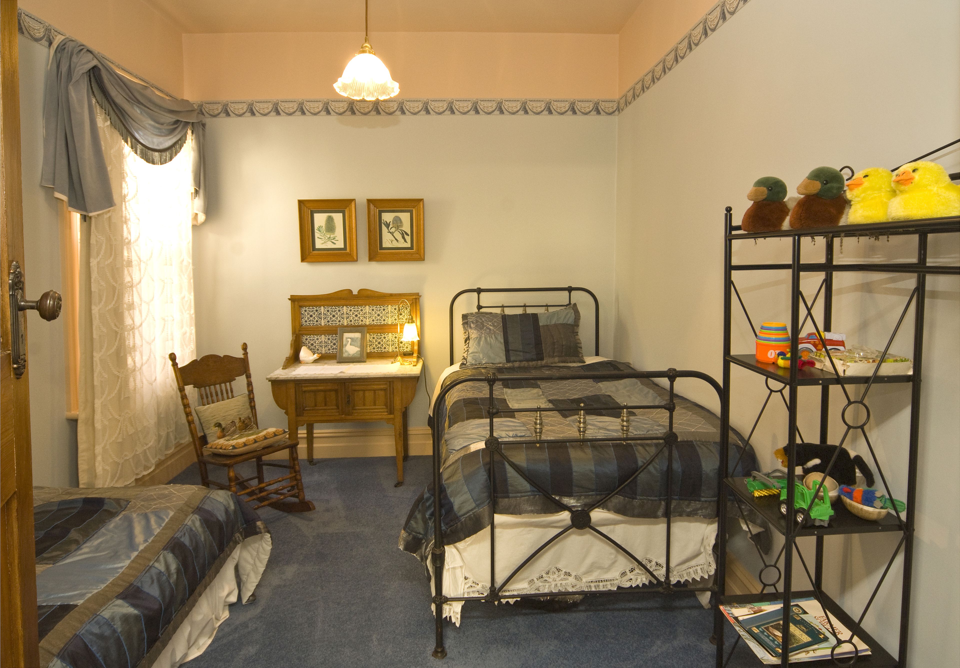 A bedroom with a bed, a chair, a nightstand, a shelf with toys, and two framed pictures on the wall.