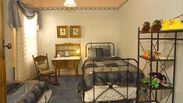 A bedroom with a bed, a chair, a nightstand, a shelf with toys, and two framed pictures on the wall.