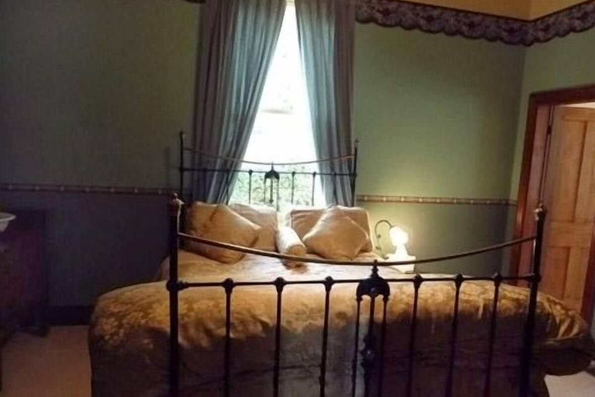 A room with a metal bed frame, a window with curtains, and a door.