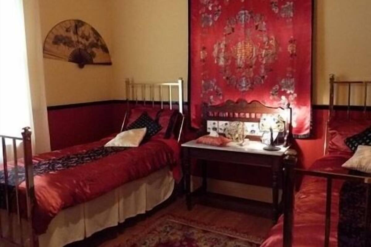 A room with two single beds, a small table, and a red tapestry on the wall.