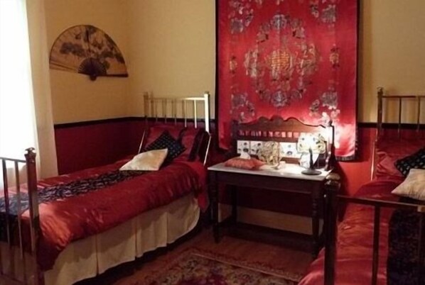 A room with two single beds, a small table, and a red tapestry on the wall.