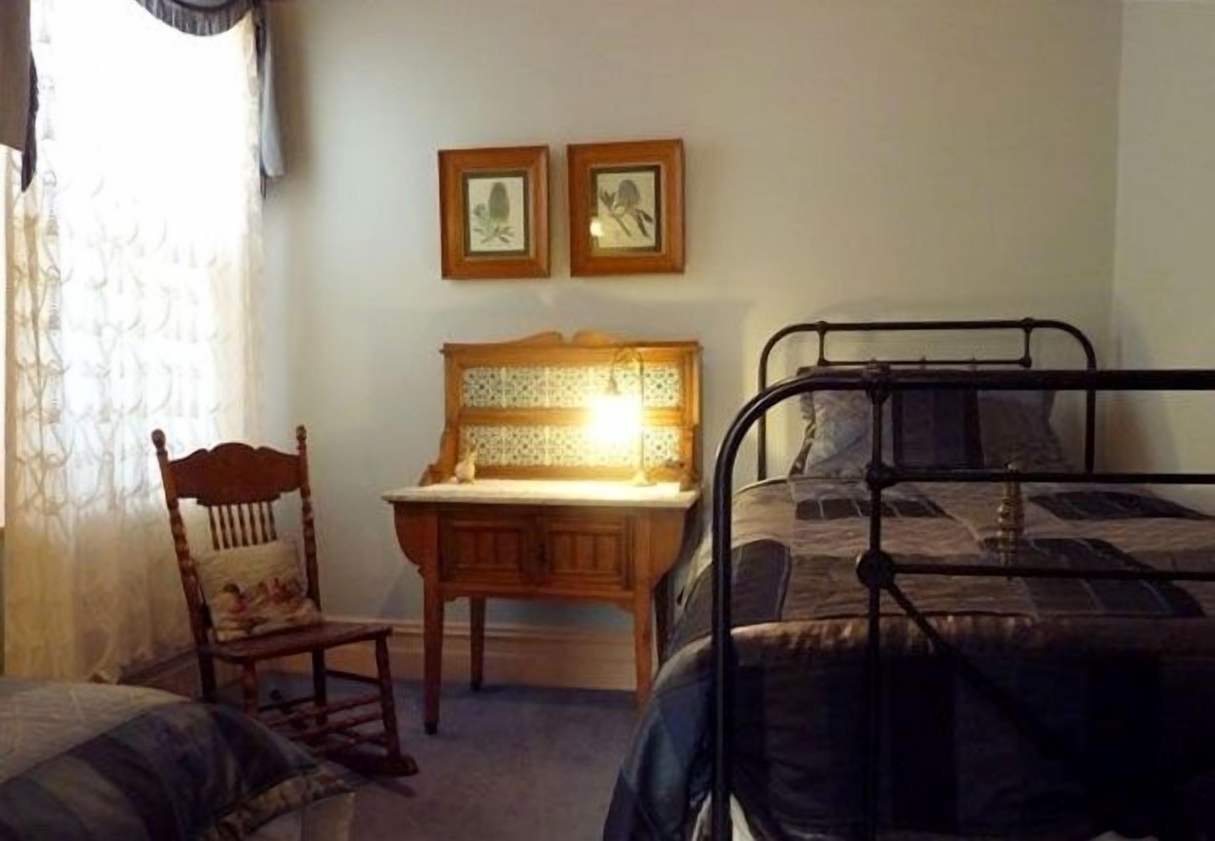 Un dormitorio con una cama, una silla, un escritorio y dos cuadros en la pared.