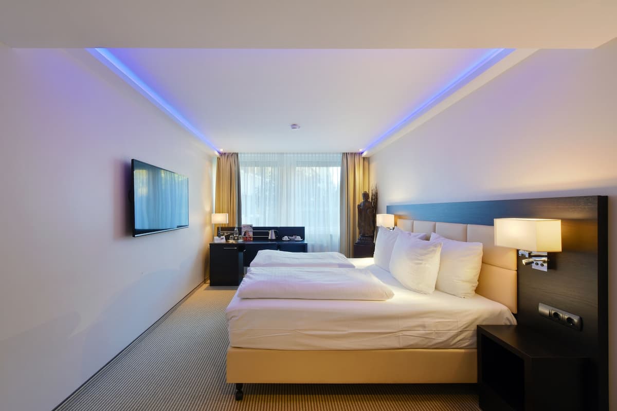 A hotel room with a large bed, a desk, and a TV mounted on the wall.