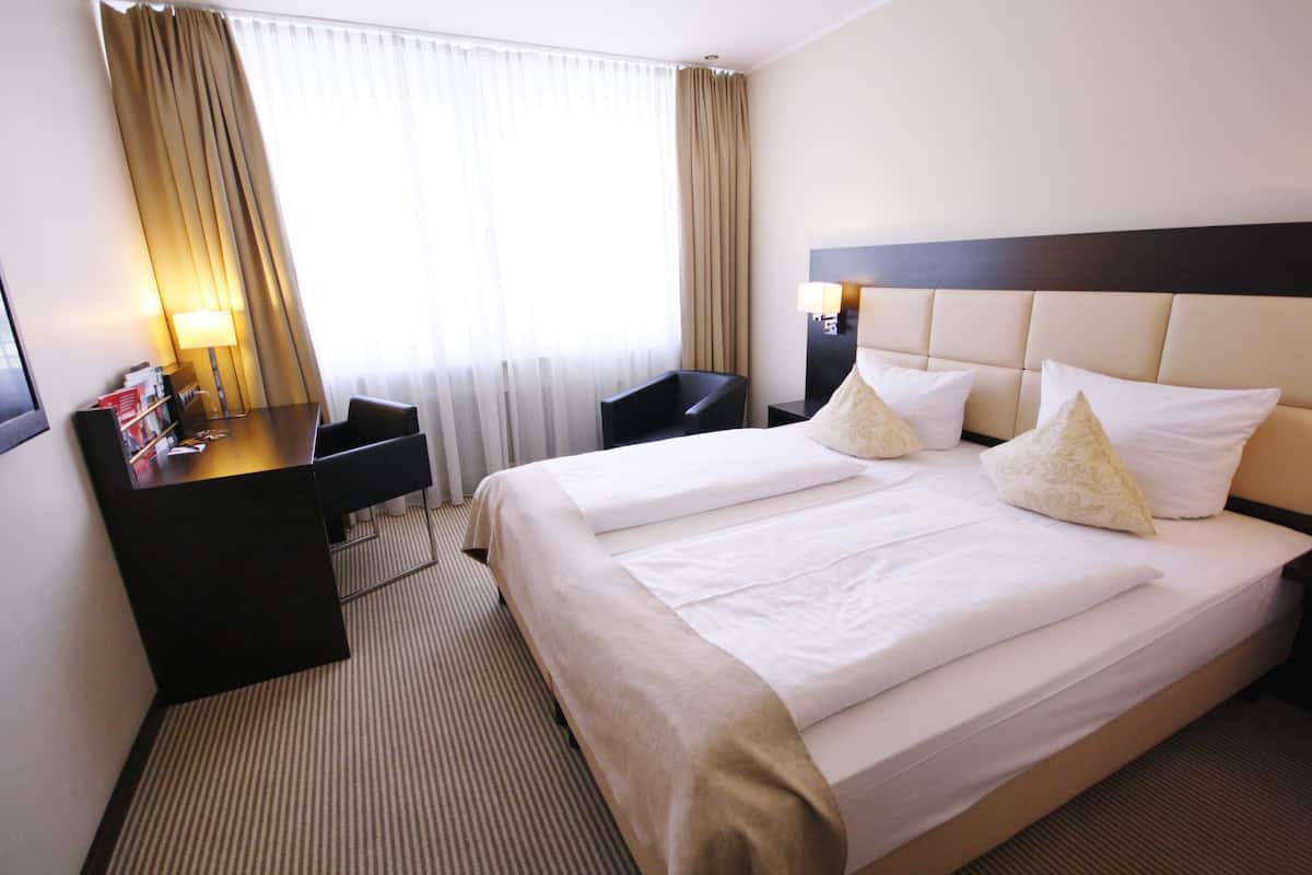 A hotel room with two beds, a desk, a chair, and a lamp.