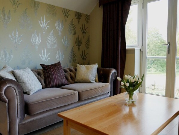 A living room with a brown leather sofa, a wooden coffee table, and a window with curtains.