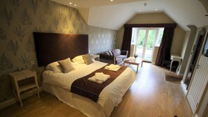 A spacious bedroom with a large bed, a wooden floor, a sofa, and a view of the outdoors. - The Sun Inn (Swindon)