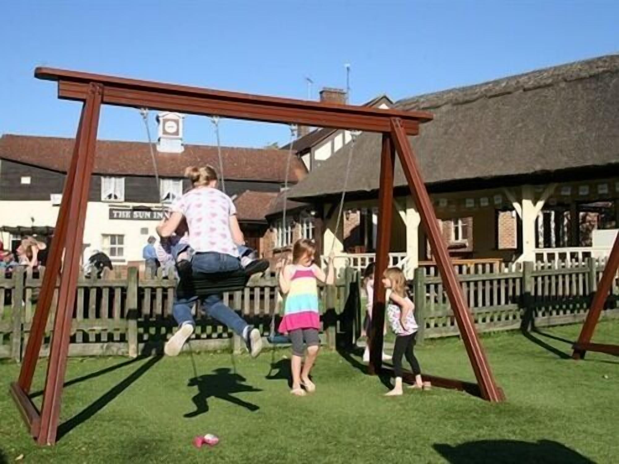 A wooden swing set in a grassy area with a building in the background.