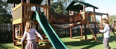 A wooden playground with a slide and climbing structures.