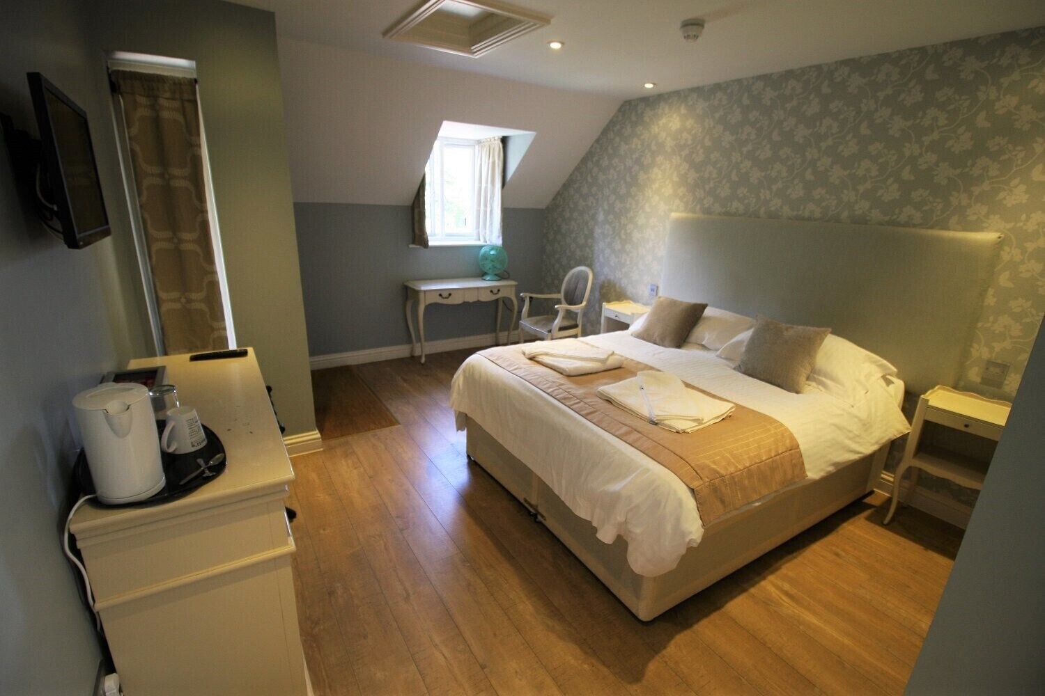 A neatly arranged bedroom with a bed, bedside table, and a desk with a chair.