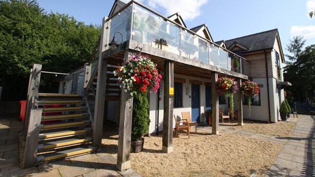 A two-story building with a balcony, wooden steps, and hanging flower baskets. - The Sun Inn (Swindon)
