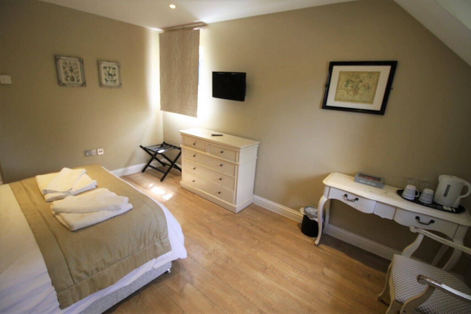 A bedroom with a bed, a dresser, a desk with a chair, and a TV mounted on the wall.