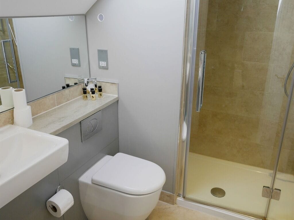 Un baño moderno con cabina de ducha de vidrio, inodoro blanco y tocador con artículos de aseo.