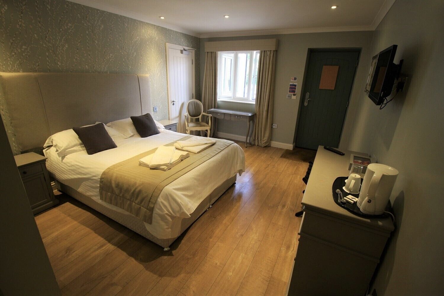 Una habitación de hotel con cama, mesita de noche, silla, escritorio y cafetera.