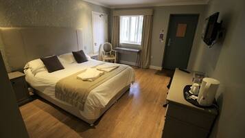 Una habitación de hotel con cama, mesita de noche, silla, escritorio y cafetera.