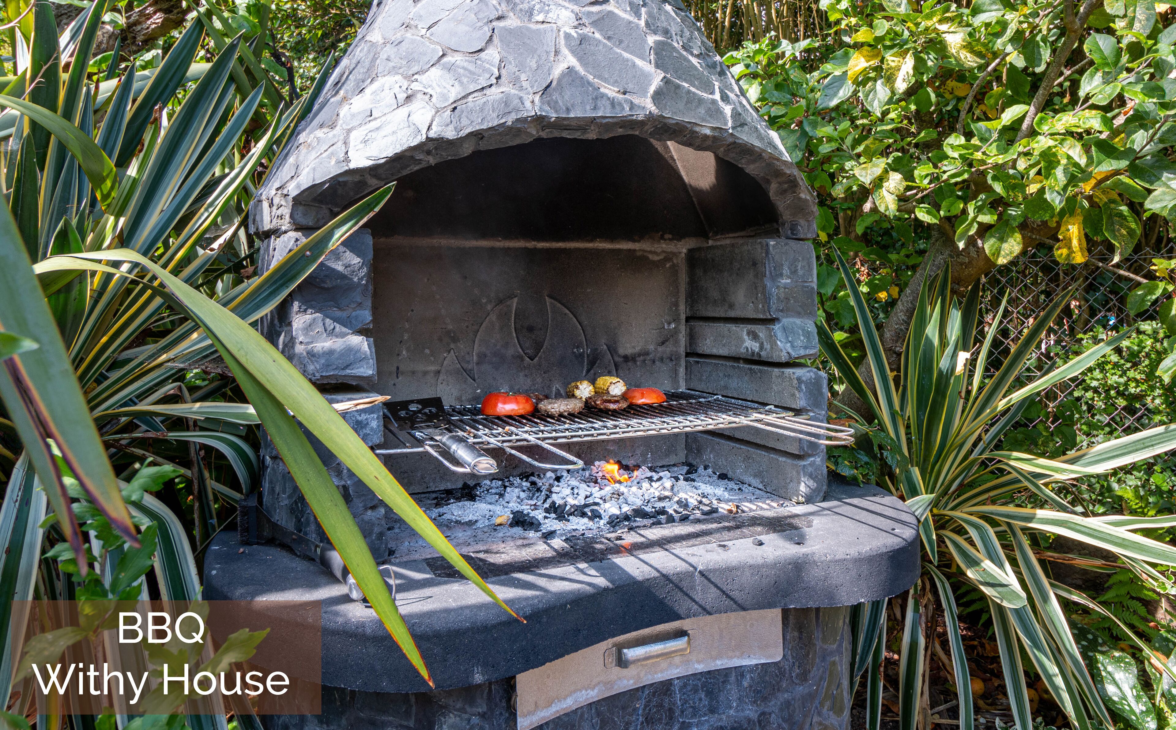 Una barbacoa de piedra al aire libre con parrilla, rodeada de vegetación.