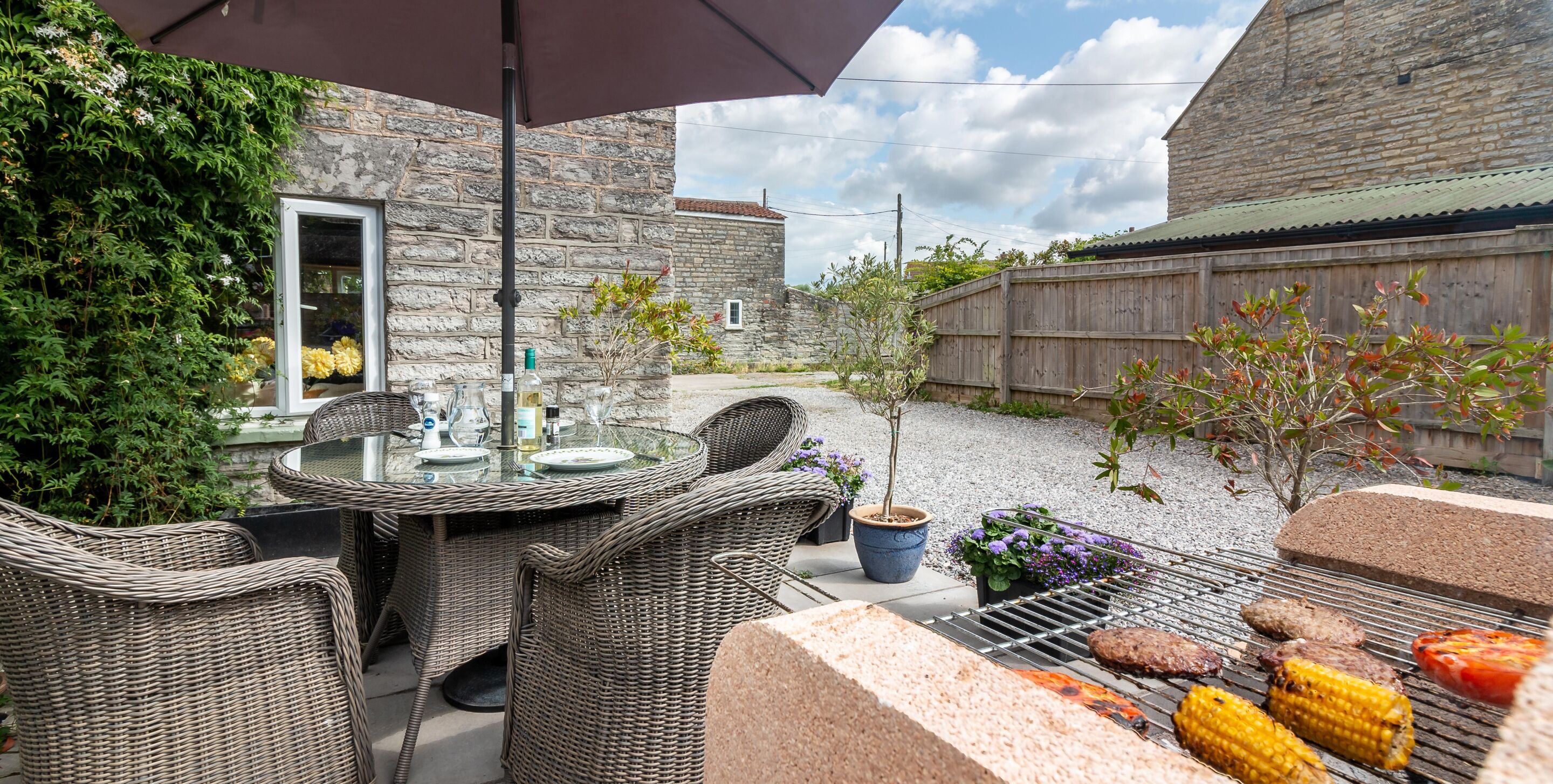 Une terrasse extérieure avec des meubles en osier, un barbecue et un bâtiment en pierre en arrière-plan.