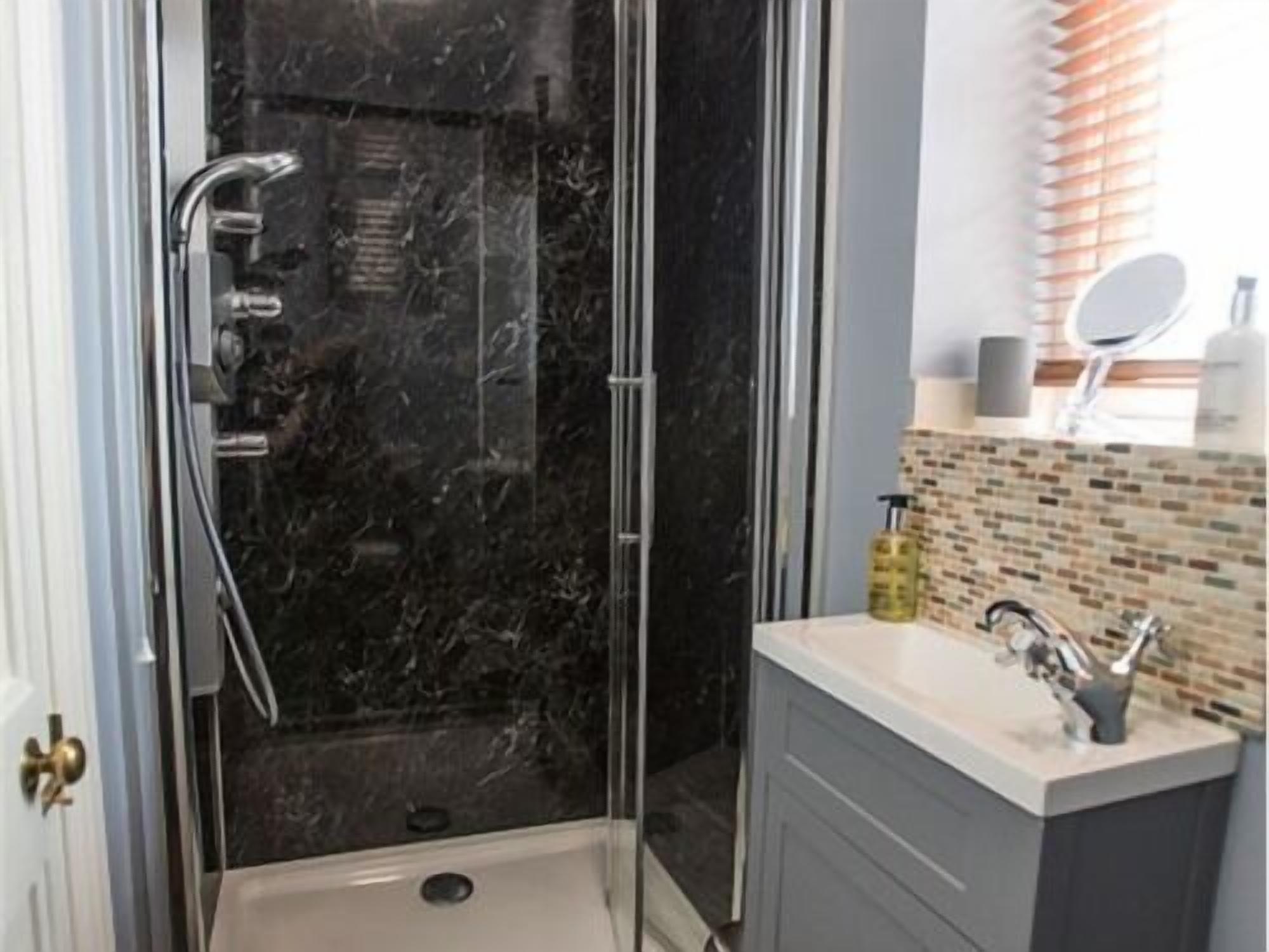 A modern bathroom with a glass-enclosed shower, a marble backsplash, and a vanity with a mirror.