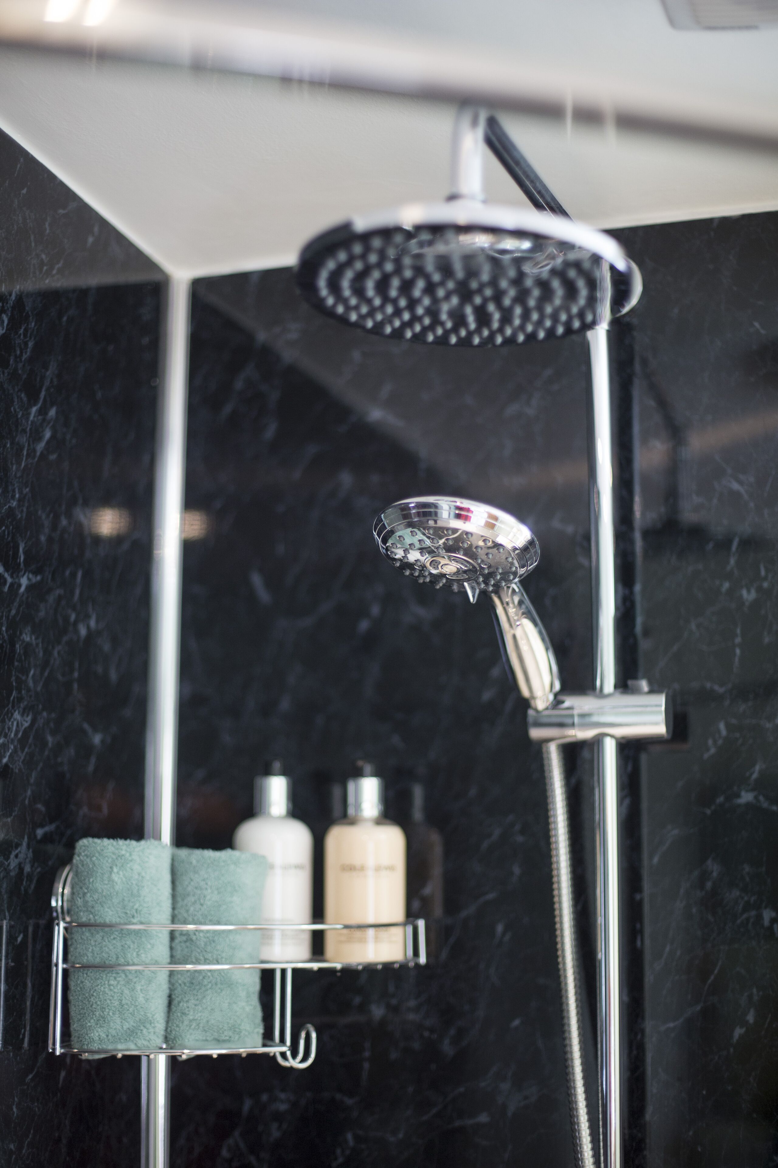 A modern bathroom with a shower, marble walls, and a towel rack with bottles.