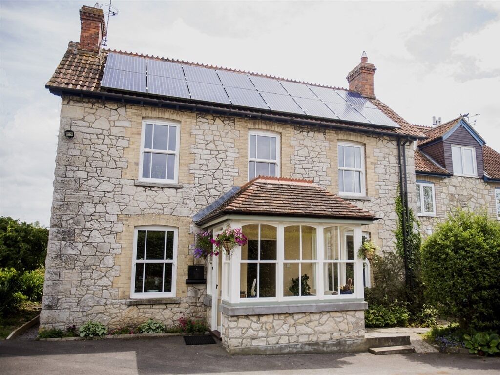 A stone house with a bay window, solar panels, and a small garden.