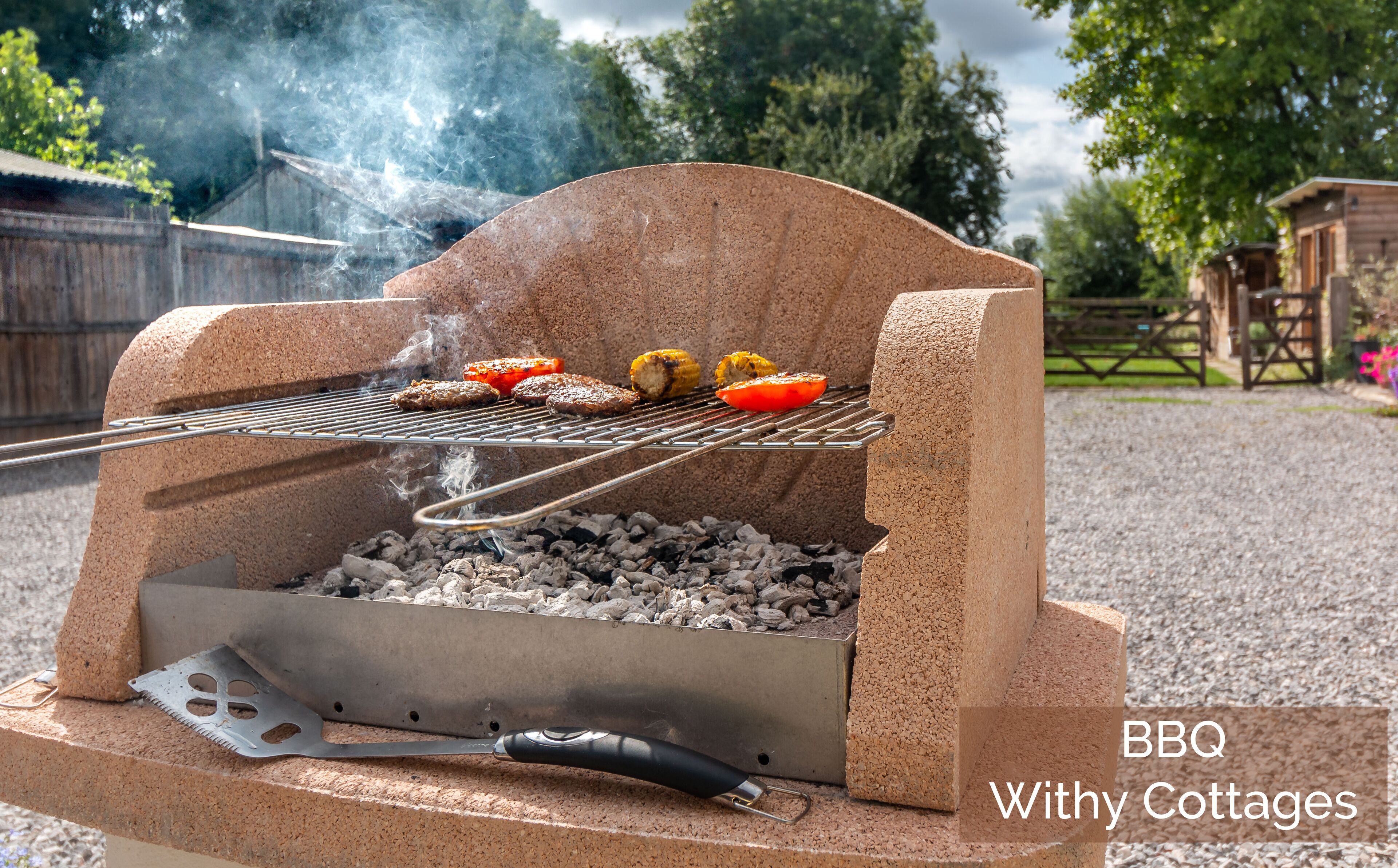 Una parrilla para barbacoa con comida cocinándose, rodeada de grava y cercas de madera.