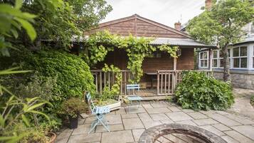 A wooden house with a covered porch, a fire pit, and potted plants.