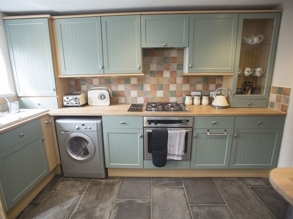 A compact kitchen with light green cabinets, a washing machine, a stove, and a microwave.