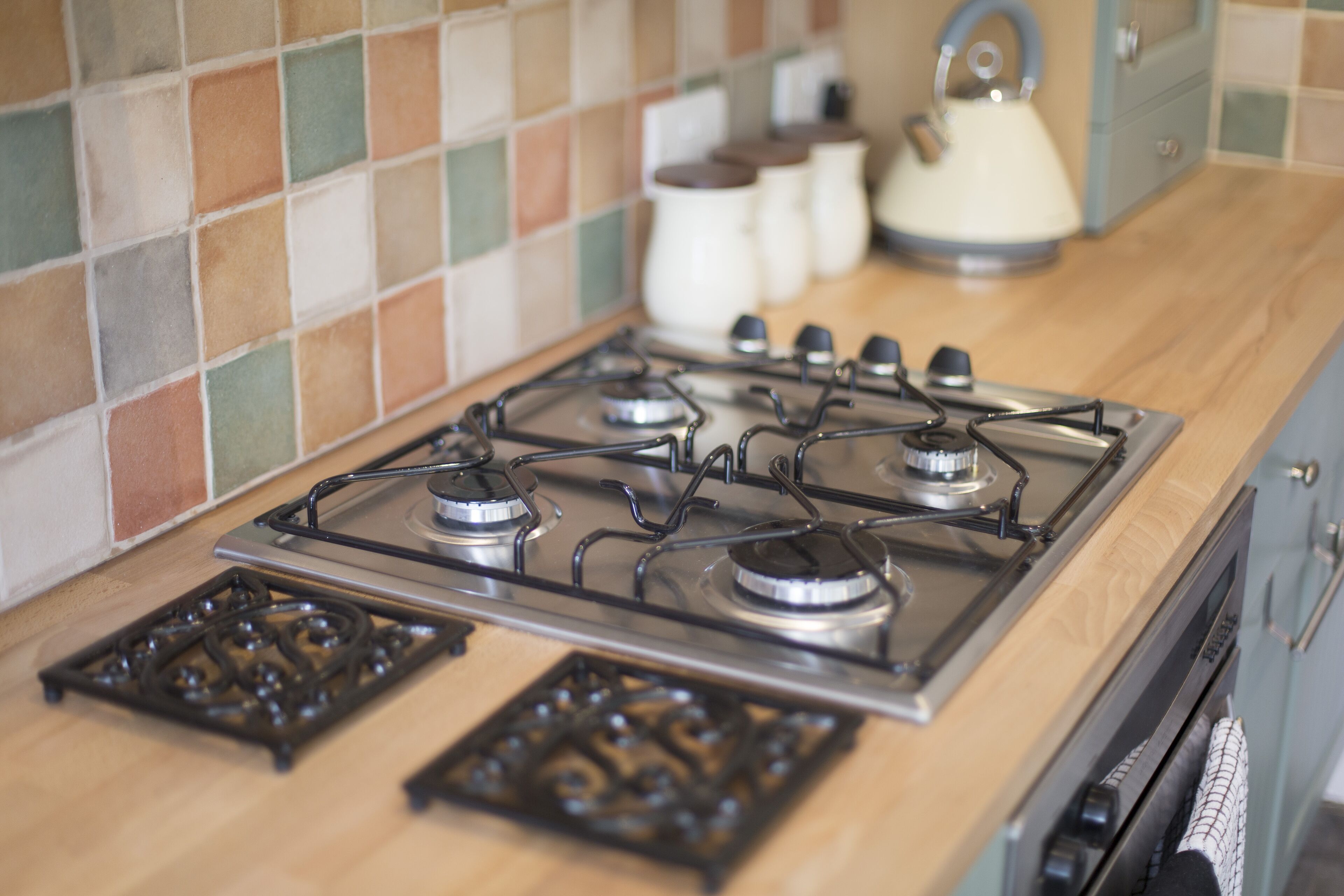 A kitchen with a gas stove, a kettle, and a tiled backsplash.