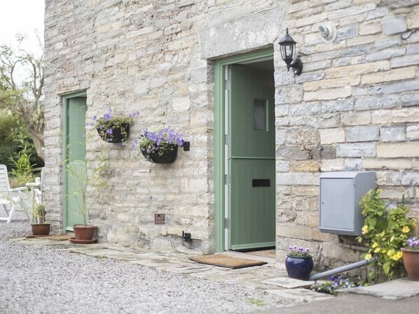 A stone building with two green doors, potted plants, and a wall-mounted light fixture. - Withy Cottages (Langport)