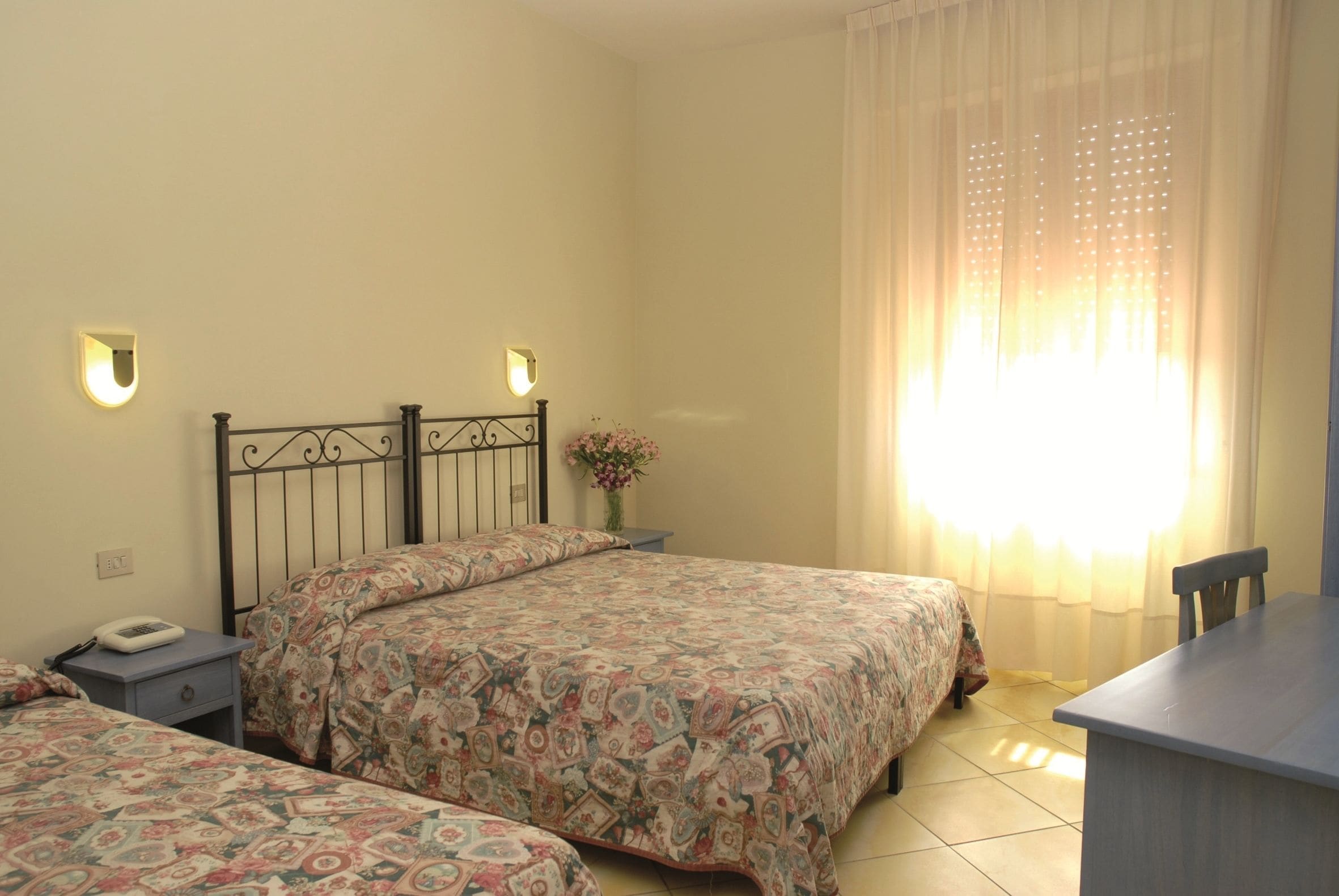 Un dormitorio con dos camas, una mesita de noche, un escritorio y una ventana con cortinas.